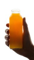 Hand holding glass bottle filled with golden orange juice or beverage against white background, isolated for packaging, advertising, and commercial design use.