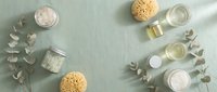 Spa and wellness products arranged flat lay with natural ingredients, bath salts, sponges, oils and eucalyptus leaves on sage green background for beauty and skincare.