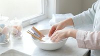 Professional chef hands whisking eggs in white ceramic bowl on kitchen counter near window with natural lighting for culinary cooking preparation.