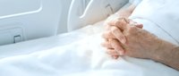 Elderly patient hands clasped together in hospital bed showing comfort and hope during medical care and recovery process.