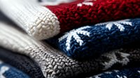 Cozy knitted winter sweaters in red, white, blue and gray colors stacked in pile, showing detailed wool texture pattern and warm fabric material for cold season.