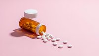 Orange prescription bottle with white pills spilled on pink background for healthcare and medication concepts.