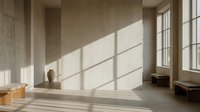 Minimalist interior with natural sunlight streaming through large windows creating geometric shadows on wooden floor and neutral walls.