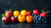 Fresh seasonal fruits arranged in row on dark background - apples, oranges, strawberry and blueberries with green leaves create vibrant healthy food composition.