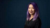 Young Asian businesswoman with purple hair smiling confidently in black blazer against dark blue background for corporate and professional marketing materials.