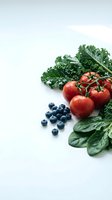 Fresh organic vegetables and berries on white background featuring kale, cherry tomatoes, blueberries and spinach for healthy eating and nutrition content.
