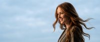Happy young Caucasian businesswoman with flowing brown hair against blue sky background, professional portrait for corporate and lifestyle content.
