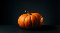 Fresh orange pumpkin with natural stem on dark background for autumn harvest, Halloween decoration, and seasonal cooking projects.