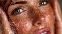 Young woman with freckles applying facial scrub exfoliant to wet skin during skincare routine. Natural beauty treatment for healthy glowing complexion.