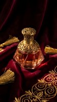 Luxury ornate perfume bottle with golden filigree cap on burgundy velvet fabric with gold tassels and embroidered details for premium fragrance branding.