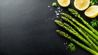 Fresh green asparagus spears with lemon slices and sea salt on dark slate background, raw organic vegetables for healthy cooking and food styling.