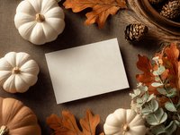 Blank card mockup with autumn decorations including white pumpkins, fall leaves, pine cones and eucalyptus on neutral beige background.
