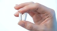 Hand holding two white capsules or pills between fingers on clean background for medical and healthcare concepts.