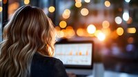 Young blonde businesswoman working on laptop in modern office with warm bokeh lights creating cozy evening atmosphere for productivity and focus.