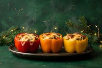 Three colorful stuffed bell peppers with melted cheese on dark plate, surrounded by pine branches and warm lights for festive holiday cooking and dining.