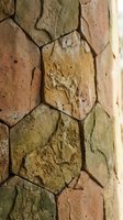 Close-up of stacked stone wall with varied earth tones, weathered texture, and natural color variations from tan to green moss. Suitable for backgrounds, construction, architecture, and design projects.