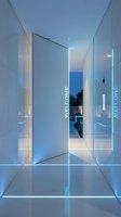 Futuristic white entrance hallway with glowing blue LED strip lights and welcome text, leading to an outdoor garden at dusk.