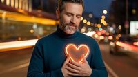 Middle-aged Caucasian man holding glowing heart symbol on city street at night with bokeh lights background for love and romance concepts.