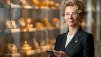 Confident mature Caucasian businesswoman in formal attire holding digital tablet against luxury jewelry store display, professional corporate portrait.