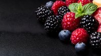 Fresh mixed berries with mint leaf on dark background, macro shot of ripe blackberries, raspberries and blueberries with water drops, copy space for text.