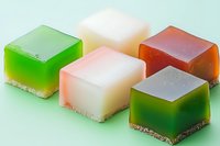 Colorful layered jelly desserts with cream and cookie base on mint green background. Assorted flavors of gelatin squares showcase gradient effect.