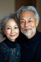 Senior Asian couple smiling at camera, wearing elegant dark clothing. Woman in patterned dress and man with gray beard in turtleneck sweater share intimate moment.