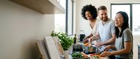 Diverse group of friends cooking together in modern kitchen, preparing healthy meal with fresh vegetables, teamwork and culinary collaboration concept.