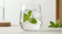 Refreshing sparkling water with fresh mint leaves in clear glass on kitchen counter. Healthy hydration beverage for wellness and detox lifestyle.