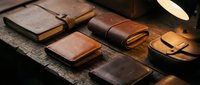 Handcrafted leather goods collection featuring wallets, notebooks and accessories on rustic wooden surface. Artisan craftsmanship for luxury lifestyle branding.