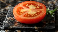 Fresh ripe tomato slice on dark stone cutting board showing detailed inner texture and seeds with natural lighting, garnished with herbs.