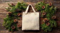 Eco-friendly canvas tote bag surrounded by festive pine branches and cones on rustic wooden background for sustainable holiday shopping and gifts.