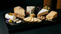 Gourmet cheese platter with assorted artisanal cheeses, crackers, nuts and grapes on dark slate board for entertaining and fine dining experiences.