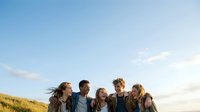 Young diverse group of friends standing together on grassy hillside outdoors, enjoying leisure time and bonding during golden hour sunset, suitable for lifestyle and social content.