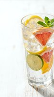 Refreshing citrus infused water with grapefruit, lemon, lime slices and fresh mint in tall glass on white wooden background for healthy hydration.