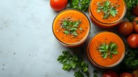 Fresh tomato gazpacho soup in bowls with parsley garnish and cherry tomatoes on white marble background for healthy cooking recipes.