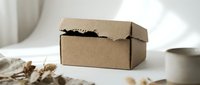 Small brown cardboard shipping box with black tissue paper on white table with dried flowers and coffee cup for e-commerce packaging mockup.