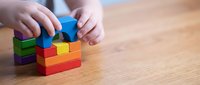 Child hands building colorful wooden block tower on table developing fine motor skills and creativity through educational play activity.