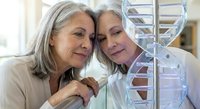 Two mature Caucasian female scientists examining DNA double helix model in modern laboratory, representing genetic research and medical discovery collaboration.