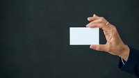 Caucasian male hand holding blank white business card against dark background for corporate branding and professional networking purposes.