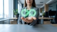 Young woman with long brown hair, wearing a gray blazer, holding a glowing green infinity symbol in her hands at a modern office desk. Represents sustainability, circular economy, and renewable business concepts.
