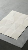 Crumpled white paper sheet with geometric fold lines on concrete surface for texture and design projects.