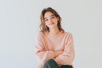 Young Asian woman in pink oversized sweater smiling confidently against white background. Natural makeup, casual style portrait showing genuine happiness and contentment.