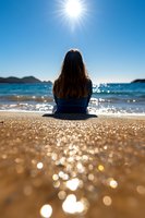 Young woman with long dark hair sitting alone on sandy beach, facing ocean waves and bright sun. Sparkling bokeh effect on sand creates magical atmosphere.