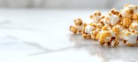 Fresh caramel popcorn scattered on white surface with selective focus and copy space, golden kernels creating appetizing snack composition.