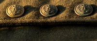 Three golden military uniform buttons with anchor emblems on textured fabric surface creating shadows in warm lighting for fashion design projects.