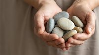 Hands gently holding collection of smooth river stones and pebbles in cupped palms for meditation, spa treatments, and natural healing practices.