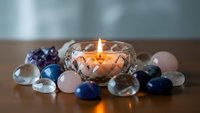 Lit candle in crystal holder surrounded by colorful gemstones and glass spheres creating peaceful meditation atmosphere for wellness and relaxation.