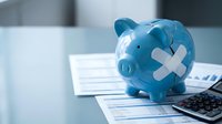 Blue piggy bank with white medical cross symbol on office desk with financial documents and calculator for healthcare savings and medical expenses planning.