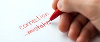 Hand holding red pen crossing out word mistake and writing correction on white paper for proofreading and editing concept.