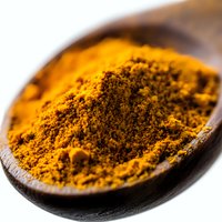 Ground turmeric powder in wooden spoon macro shot on white background, bright yellow-orange spice used in cooking and traditional medicine, selective focus.